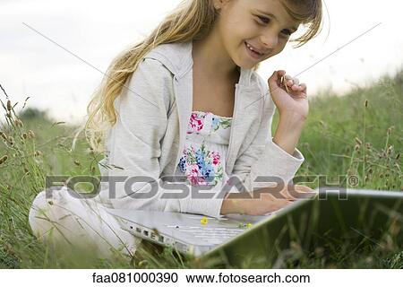 Stock Image - Girl sitting in grass, using laptop computer. Fotosearch