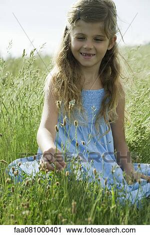 Stock Image - Girl sitting on grass picking flowers. Fotosearch