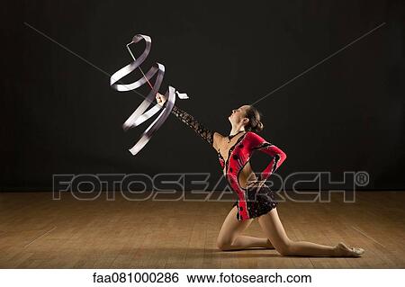 Stock Photograph - Gymnast kneeling on floor twirling ribbon. Fotosearch