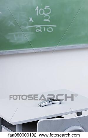 Stock Image - Handgun on desk in school classroom. Fotosearch