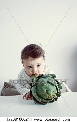 Picture - Infant biting into artichoke stem, portrait. Fotosearch