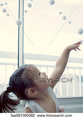 Stock Image - Little girl looking up at pompom garland. Fotosearch