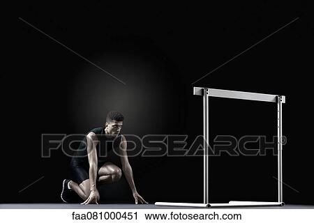 Stock Image - Male athlete at starting position in front of hurdle. Fotosearch