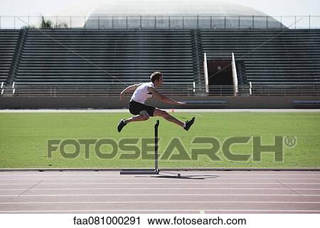 Stock Image - Male athlete clearing hurdle, side view. Fotosearch