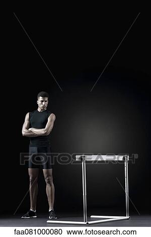 Male athlete standing by hurdle View Large Photo Image Stock Image - Male athlete standing by hurdle. Fotosearch