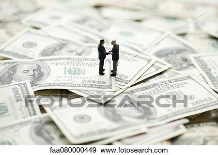 Male figurines shaking hands on pile of one hundred dollar bills View Large Photo Image Stock Photo - Male figurines shaking hands on pile of one hundred dollar bills. Fotosearch