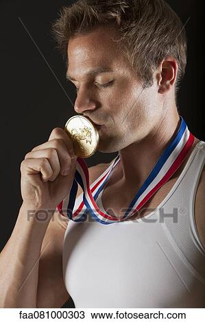 Stock Image - Male gymnast kissing gold medal, portrait. Fotosearch