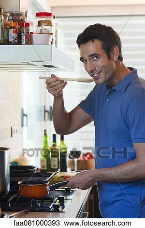 Stock Image - Man cooking in kitchen, smiling at camera. Fotosearch
