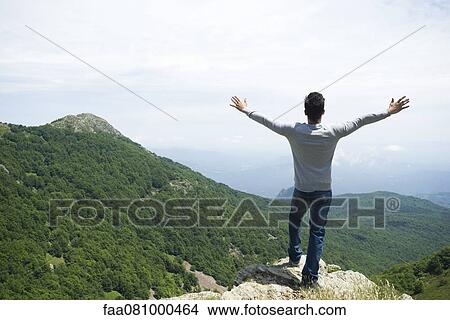 Man standing on rock looking at mountainscape View Large Photo Image Picture - Man standing on rock looking at mountainscape. Fotosearch