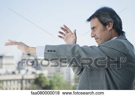 Mature businessman holding arms out in front of him and pointing, looking out of frame View Large Photo Image Stock Photo - Mature businessman holding arms out in front of him and pointing, looking out of frame. Fotosearch