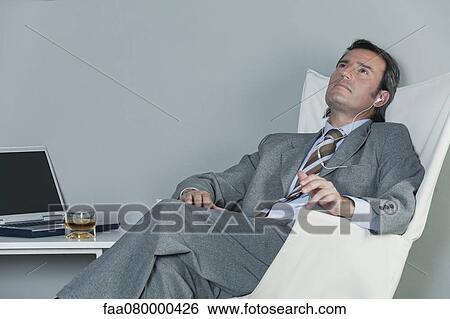 Mature businessman relaxing on chair with earphones View Large Photo Image Stock Photograph - Mature businessman relaxing on chair with earphones. Fotosearch