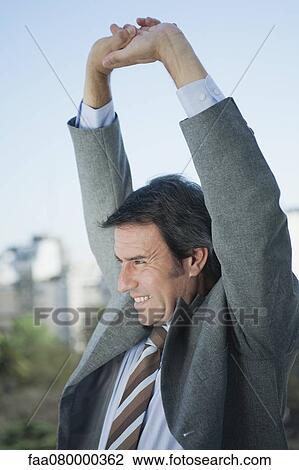 Stock Image - Mature businessman stretching arms outdoors. Fotosearch