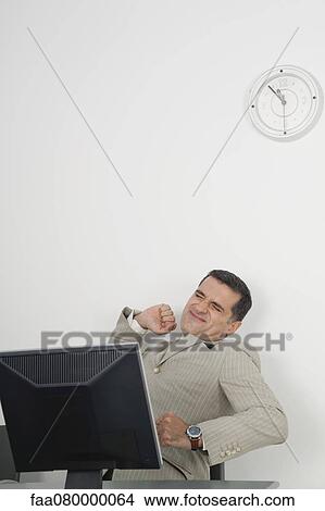 Picture - Mature businessman stretching at desk. Fotosearch
