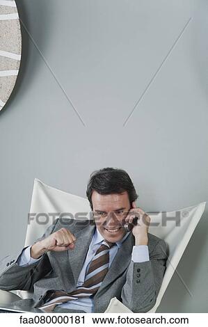 Stock Image - Mature businessman using cell phone, making fist and smiling. Fotosearch