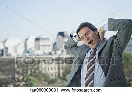 Stock Image - Mature businessman yawning and stretching outdoors. Fotosearch
