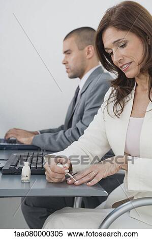 Stock Photography - Mature businesswoman applying nail polish in office. Fotosearch