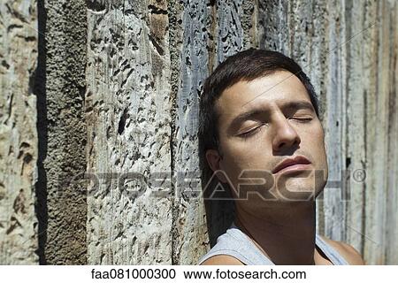 Stock Image - Mid-adult man sunbathing with eyes closed, portrait. Fotosearch