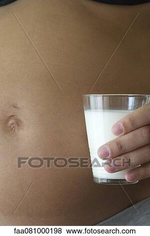 Pregnant woman holding glass of milk beside stomach, cropped View Large Photo Image Stock Photo - Pregnant woman holding glass of milk beside stomach, cropped. Fotosearch