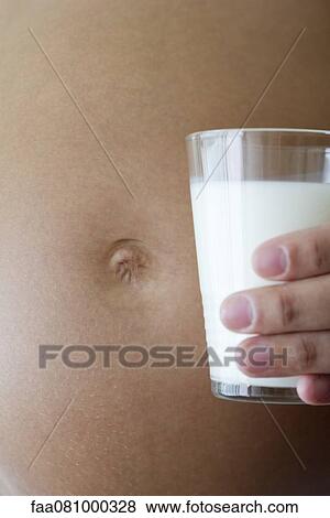 Stock Photo - Pregnant woman holding glass of milk beside stomach, cropped. Fotosearch