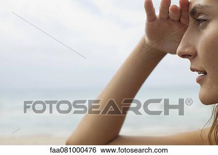 Stock Photograph - Woman at the beach, shading eyes and looking away. Fotosearch