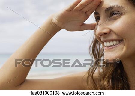 Stock Photo - Woman at the beach, shading eyes to look at view. Fotosearch
