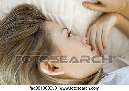 Stock Image - Woman lying down, looking away in thought. Fotosearch