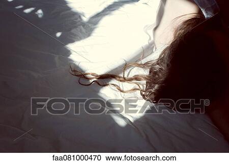 Stock Image - Woman lying on bed, cropped. Fotosearch