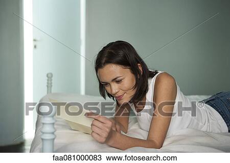 Stock Image - Woman lying on bed, reading letter. Fotosearch