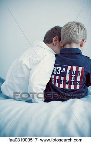 Stock Photo - Young brothers sitting side by side, rear view. Fotosearch
