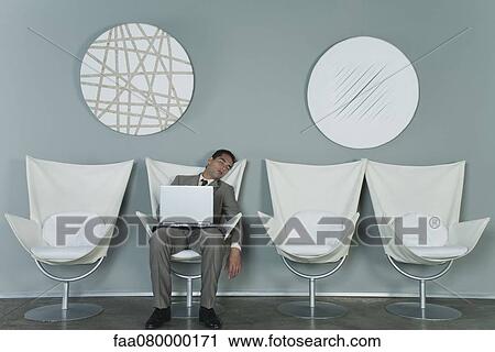 Stock Image - Young businessman asleep in armchair with laptop computer on lap. Fotosearch
