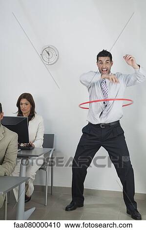 Young businessman playing with hula hoop in office while colleagues work View Large Photo Image Stock Image - Young businessman playing with hula hoop in office while colleagues work. Fotosearch