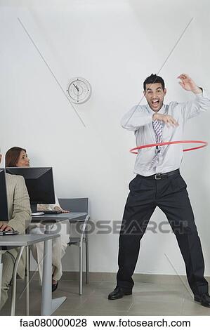 Stock Photo - Young businessman playing with hula hoop in office. Fotosearch
