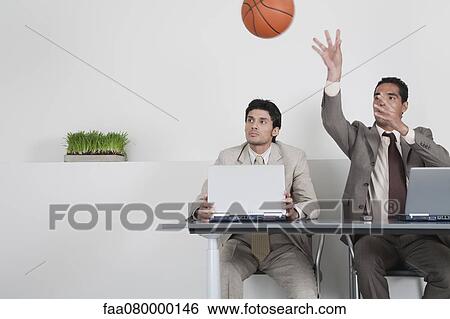 Stock Photograph - Young businessman watching colleague throwing basketball. Fotosearch