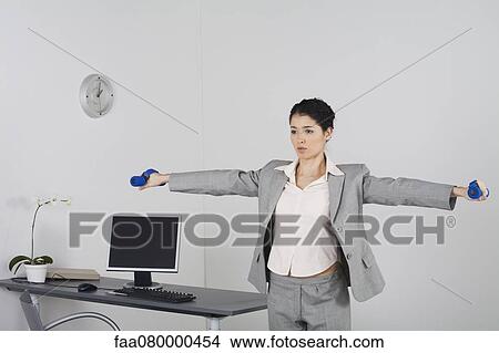 Picture - Young businesswoman exercising in office with dumbbells. Fotosearch