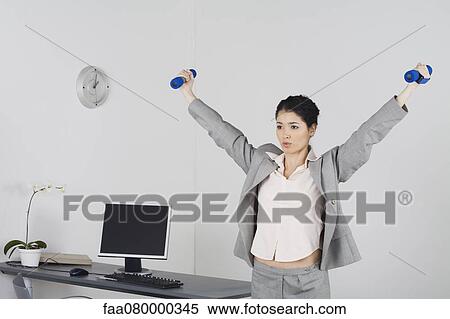 Young businesswoman exercising in office with dumbbells View Large Photo Image Stock Photography - Young businesswoman exercising in office with dumbbells. Fotosearch