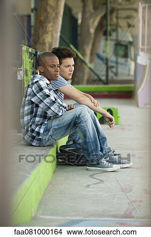 Picture - Young men sitting on sidewalk. Fotosearch