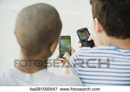 Stock Photo - Young men using cell phones, rear view. Fotosearch