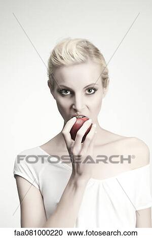 Stock Image - Young woman biting into apple, portrait. Fotosearch