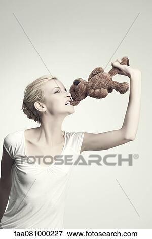 Stock Photo - Young woman biting teddy bear, portrait. Fotosearch
