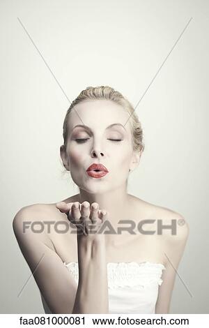 Stock Image - Young woman blowing kiss with eyes closed, portrait. Fotosearch