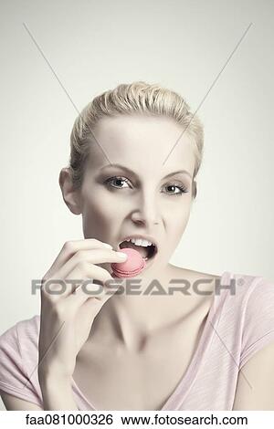 Stock Photograph - Young woman eating macaroon, portrait. Fotosearch