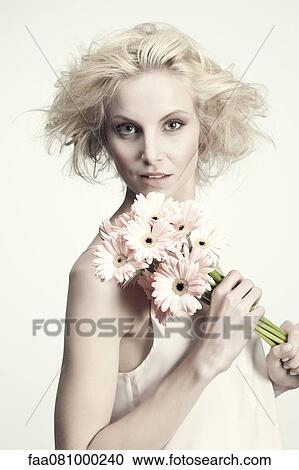 Stock Image - Young woman holding bunch of gerbera daisies, portrait. Fotosearch