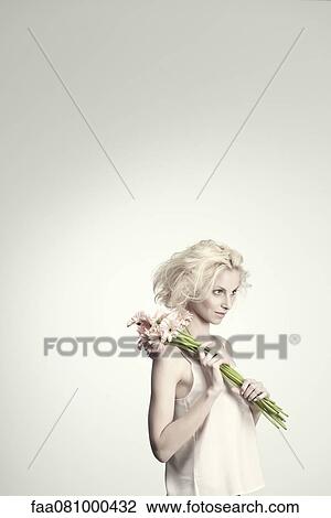 Stock Image - Young woman holding bunch of gerbera daisies, portrait. Fotosearch