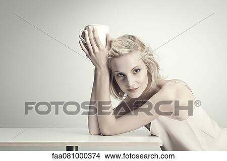 Young woman holding coffee cup at table, portrait View Large Photo Image Picture - Young woman holding coffee cup at table, portrait. Fotosearch