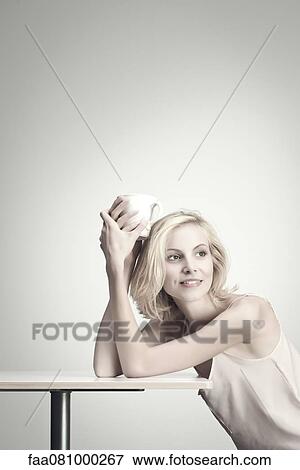 Young woman holding coffee cup at table, portrait View Large Photo Image Stock Photo - Young woman holding coffee cup at table, portrait. Fotosearch