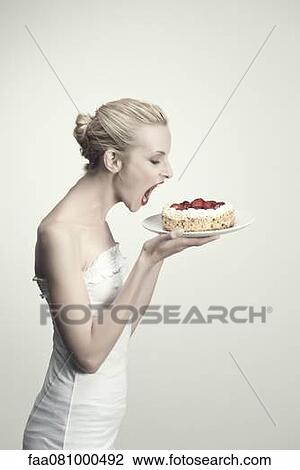 Stock Image - Young woman holding strawberry cake with open mouth, side view, portrait. Fotosearch