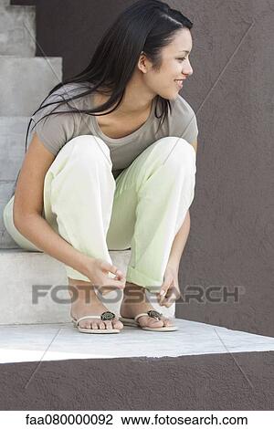 Stock Image - Young woman sitting on steps, looking away in thought. Fotosearch