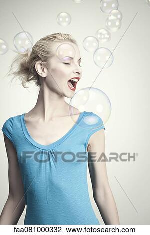Stock Image - Young woman surrounded by bubbles with mouth open. Fotosearch