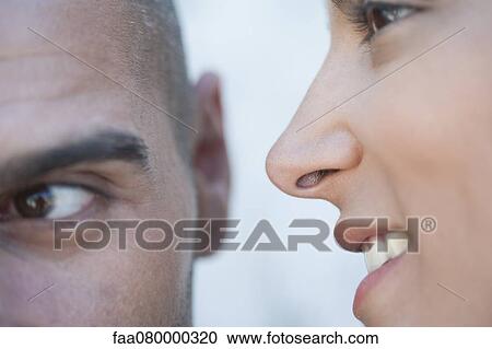 Stock Image - Young woman whispering in man's ears, cropped. Fotosearch