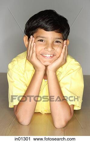 Stock Image - Boy lying on floor, hand on face. Fotosearch
